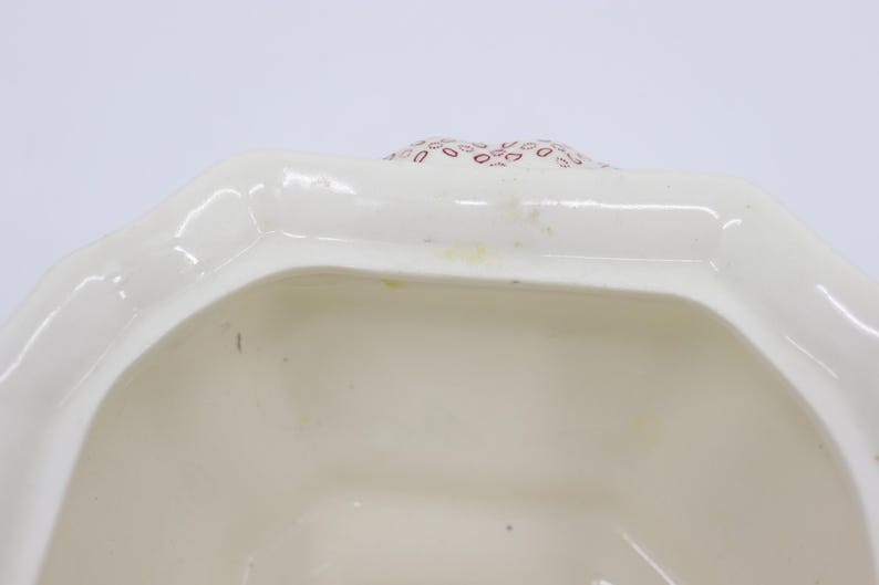 May include: White ceramic lidded jar with a red and white floral pattern. The lid is open and the inside of the jar is visible.
