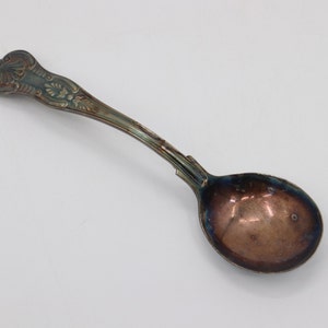 May include: A silver-plated spoon with an ornate handle and a rounded bowl. The spoon has a tarnished finish, giving it an antique look.