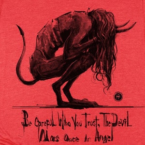 Op de afbeelding: Rood T-shirt met een zwart-witte illustratie van een demon met de tekst "Be Careful Who You Trust, The Devil Was Once An Angel".