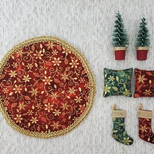 May include: A set of Christmas decorations including a red and gold round table runner, two green and gold pillows, two green and gold stockings, and two small potted green Christmas trees.