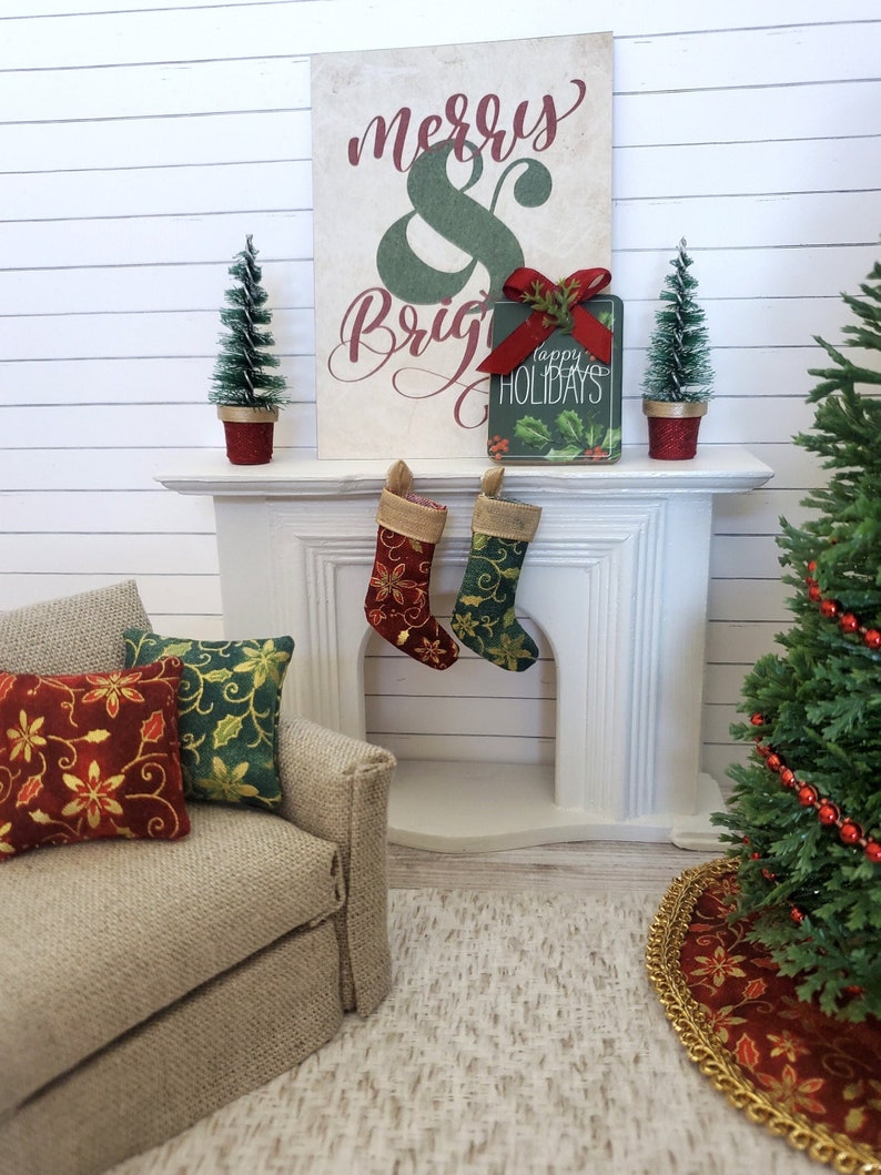 May include: A white fireplace mantel with a red and green Christmas stocking hanging on each side. A sign that says "Merry & Bright" is on the mantel, along with a small Christmas tree and a gift box that says "Happy Holidays".