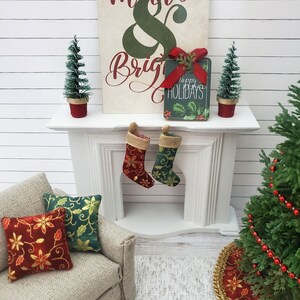 May include: A miniature Christmas scene with a fireplace, stockings, a small couch with red and green pillows, a Christmas tree with red beads, and a sign that says "Merry & Bright" with a gift that says "Happy Holidays".