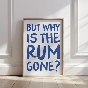 Op de afbeelding: Een ingelijst print met de tekst "But why is the rum gone?" in blauwe penseelstreken op een witte achtergrond.