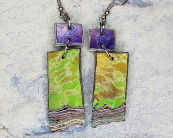 May include: A pair of dangle earrings with a layered, marbled look. The top portion of each earring is a square with a purple, blue, and green color scheme. The bottom portion of each earring is a rectangle with a green, yellow, and brown color scheme.