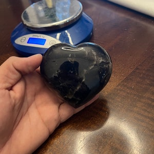 May include: A black heart-shaped stone with white veins. The stone is smooth and polished.
