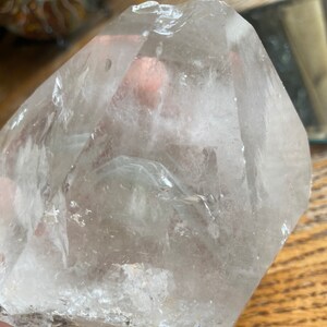 May include: A large, clear quartz crystal with a natural, rough surface. The crystal is shaped like a pyramid with a pointed top and a flat base. It has a cloudy, milky appearance with some internal inclusions.