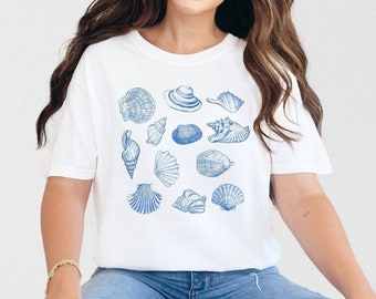 Op de afbeelding: Een wit T-shirt met een blauwe print van verschillende schelpen. De schelpen zijn symmetrisch gerangschikt.