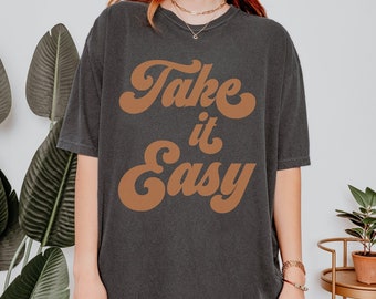 May include: An oversized t-shirt in dark grey with the text "Take it Easy" in brown retro lettering.