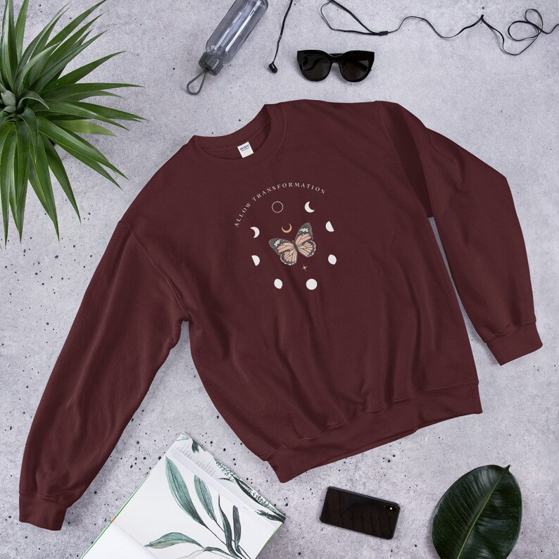 Puede incluir: Una sudadera color granate con un gr&aacute;fico de una mariposa y fases lunares. El texto "ALLOW TRANSFORMATION" est&aacute; impreso en un c&iacute;rculo alrededor de la mariposa.