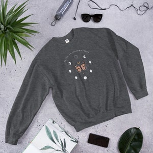 Puede incluir: Una sudadera gris oscuro con un gr&aacute;fico blanco de una mariposa y fases lunares. El gr&aacute;fico dice "Align Transformation".