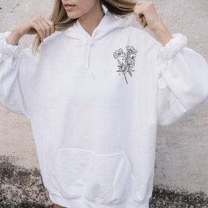 May include: White hooded sweatshirt with a black line drawing of a bouquet of flowers on the front.