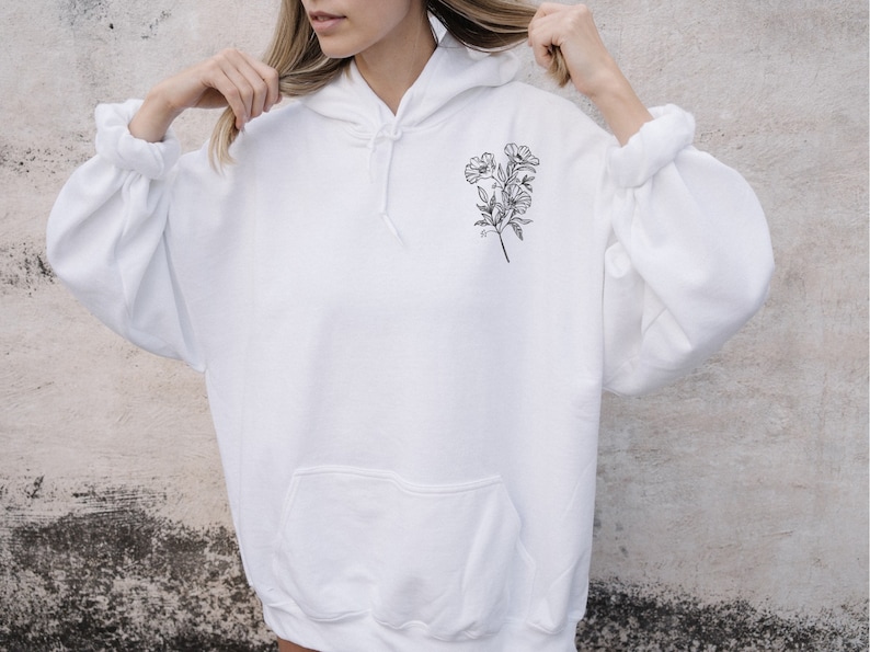 May include: White hooded sweatshirt with a black line drawing of a bouquet of flowers on the front.