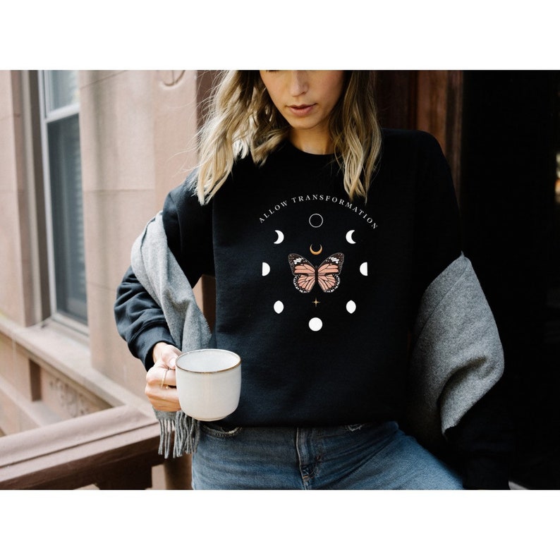 Puede incluir: Sudadera negra con un gr&aacute;fico de una mariposa y fases lunares. El texto "ALLOW TRANSFORMATION" est&aacute; impreso alrededor de las fases lunares.
