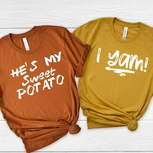 May include: Two t-shirts with a Thanksgiving-themed couple's design. The brown shirt says "He's my sweet potato" and the mustard yellow shirt says "I yam!"