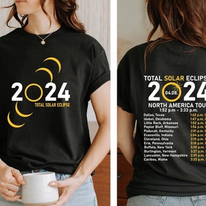 May include: Black t-shirt with a yellow graphic of the 2024 total solar eclipse. The back of the shirt lists the cities and times of the eclipse across North America.