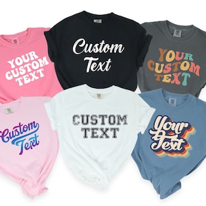 May include: Six different t-shirts with various text designs. The shirts are in different colors, including pink, white, black, gray, and blue. The text on the shirts includes "Your Custom Text", "Custom Text", and "Custom Text" in different fonts and styles.