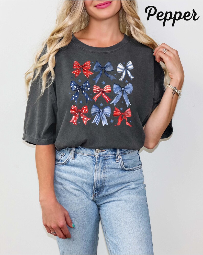 K&ouml;nnte beinhalten: Ein dunkelgraues T-Shirt mit einem Muster aus roten, wei&szlig;en und blauen Schleifen. Die Schleifen sind in einem Raster angeordnet und haben einen Aquarell-Effekt. Das Shirt hat eine lockere Passform und kurze &Auml;rmel.