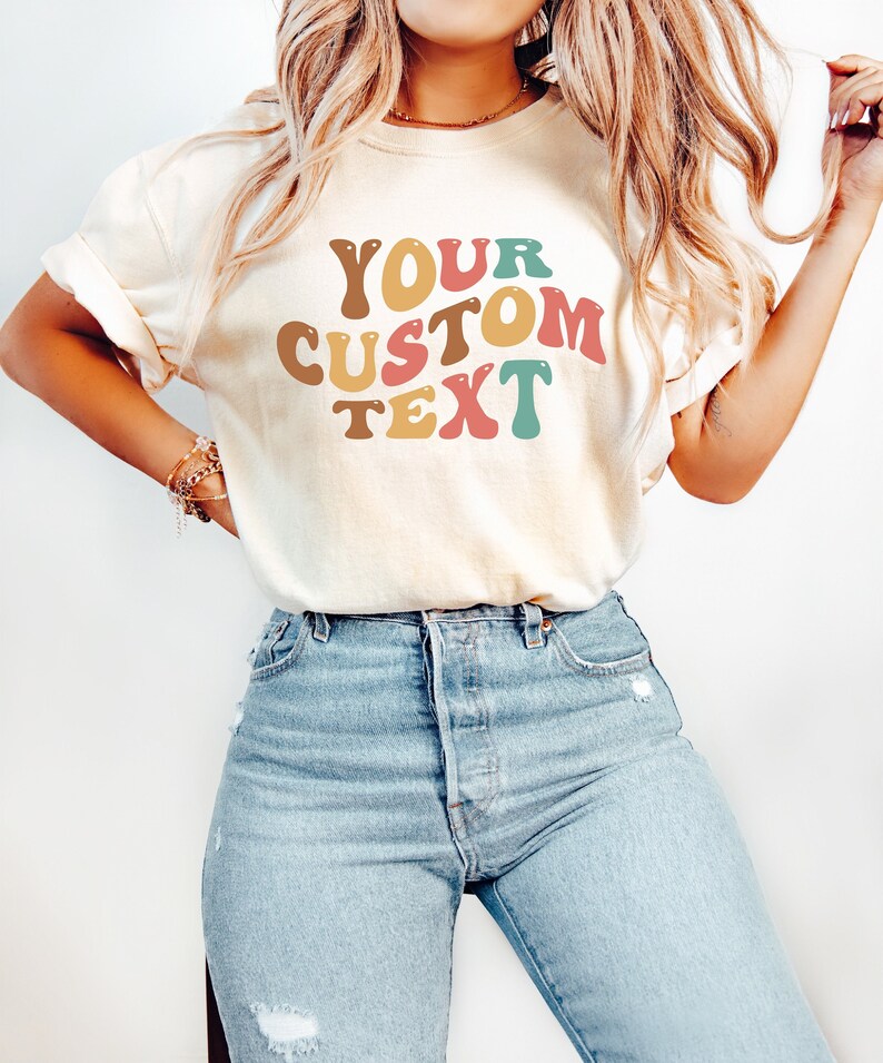 May include: A white t-shirt with the text "YOUR CUSTOM TEXT" in colourful, retro-style lettering.