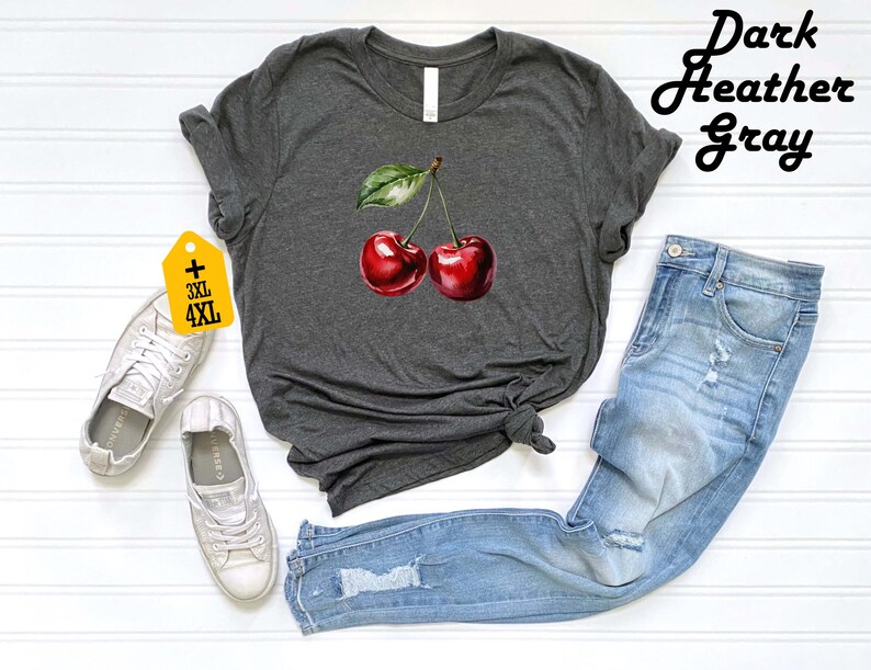 Peut inclure: T-shirt gris chin&eacute; fonc&eacute; avec une illustration &agrave; l'aquarelle de deux cerises rouges et une feuille verte. Le t-shirt est associ&eacute; &agrave; un jean en denim bleu clair et des baskets blanches. L'&eacute;tiquette indique les tailles 3XL et 4XL.