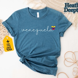May include: A blue t-shirt with the word "venezuela" in cursive script and a heart-shaped Venezuelan flag graphic. A yellow tag indicates plus sizes 3XL and 4XL. The shirt is made of a soft material.