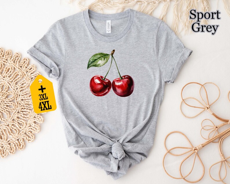 Peut inclure: T-shirt gris clair avec une illustration &agrave; l'aquarelle de deux cerises m&ucirc;res. Les cerises sont d'un rouge profond avec une feuille et une tige vertes. Le t-shirt porte le texte "Sport Grey" et une &eacute;tiquette "3XL 4XL".
