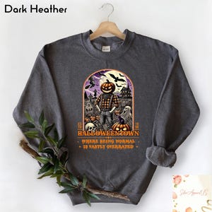May include: Dark heather grey sweatshirt with a graphic print of a pumpkin-headed figure in a graveyard. The text reads "Halloweentown, Where being normal is vastly overrated."