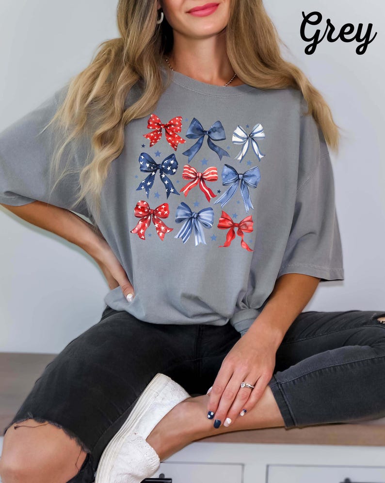 K&ouml;nnte beinhalten: Ein graues T-Shirt mit einem Design aus roten, wei&szlig;en und blauen Schleifen. Die Schleifen sind in einem Raster angeordnet und haben einen Aquarell-Effekt. Das Wort "Grey" ist in wei&szlig;er Schrift in der oberen rechten Ecke des Bildes geschrieben.
