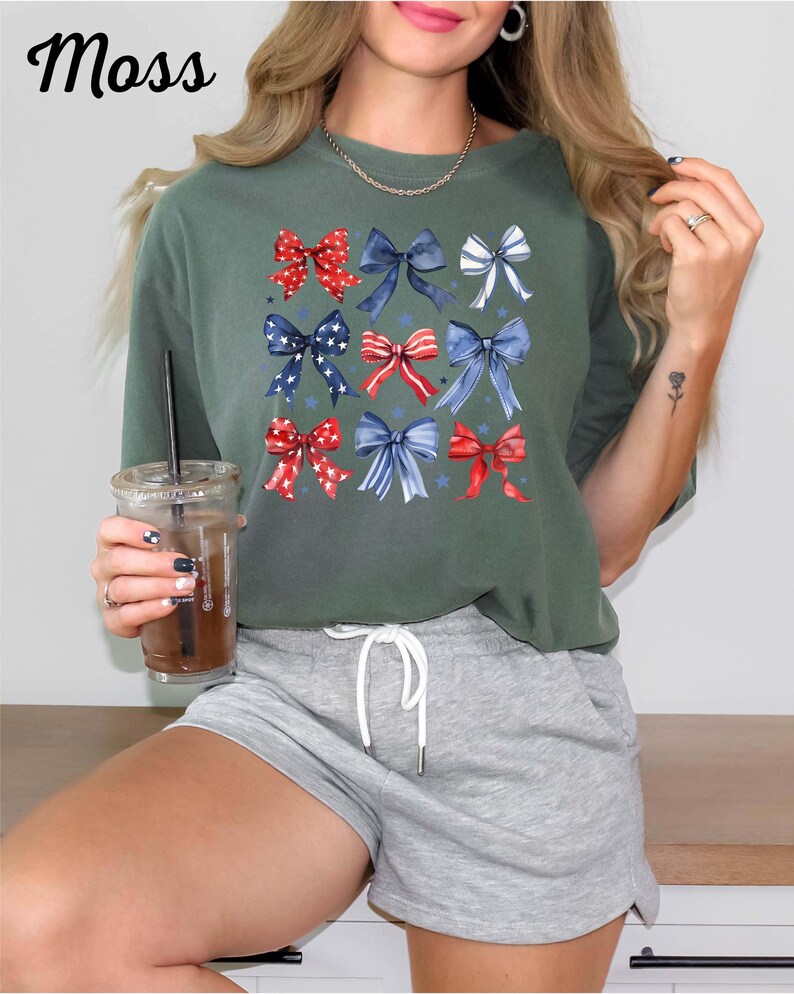 K&ouml;nnte beinhalten: Ein gr&uuml;nes T-Shirt mit kurzen &Auml;rmeln und einem Muster aus roten, wei&szlig;en und blauen Schleifen. Die Schleifen sind in einem Raster angeordnet und haben einen Aquarell-Effekt. Das Shirt wird mit grauen Shorts kombiniert.