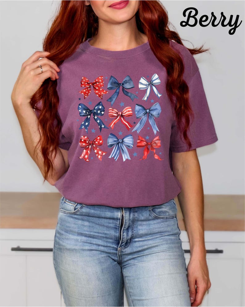 K&ouml;nnte beinhalten: Ein lilafarbenes T-Shirt mit einem Muster aus roten, wei&szlig;en und blauen Schleifen. Die Schleifen sind in einem Raster angeordnet und haben einen Aquarell-Effekt. Der Text "Berry" befindet sich in der oberen rechten Ecke des Bildes.