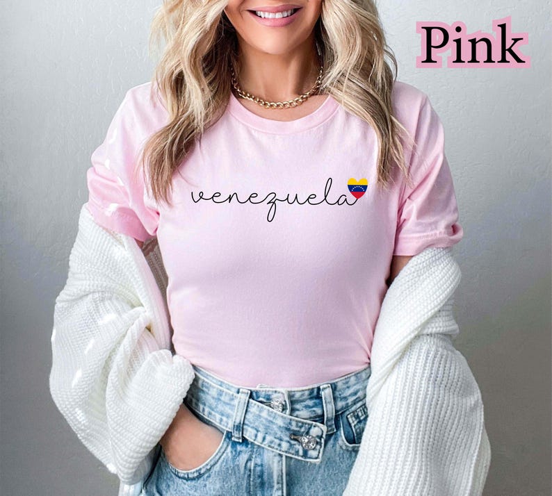 May include: A light pink t-shirt with the word "venezuela" in a cursive font. The shirt features a small heart-shaped graphic with the Venezuelan flag colors. The word "Pink" is written in a pink font in the upper right corner.