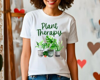 Könnte beinhalten: Weißes T-Shirt mit dem Text "Plant Therapy" in grüner Schrift. Darunter befinden sich Aquarellillustrationen verschiedener Topfpflanzen, darunter eine Monstera und eine Sukkulente. Das T-Shirt wird von einer Person getragen.