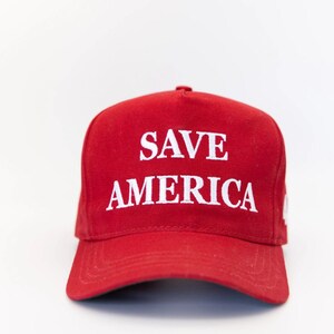 May include: A red baseball cap with a white embroidered slogan that reads "SAVE AMERICA".
