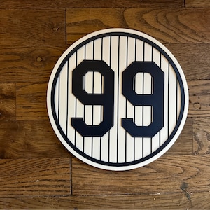 May include: A white and blue circular sign with a baseball field pattern and the number 99 in black.