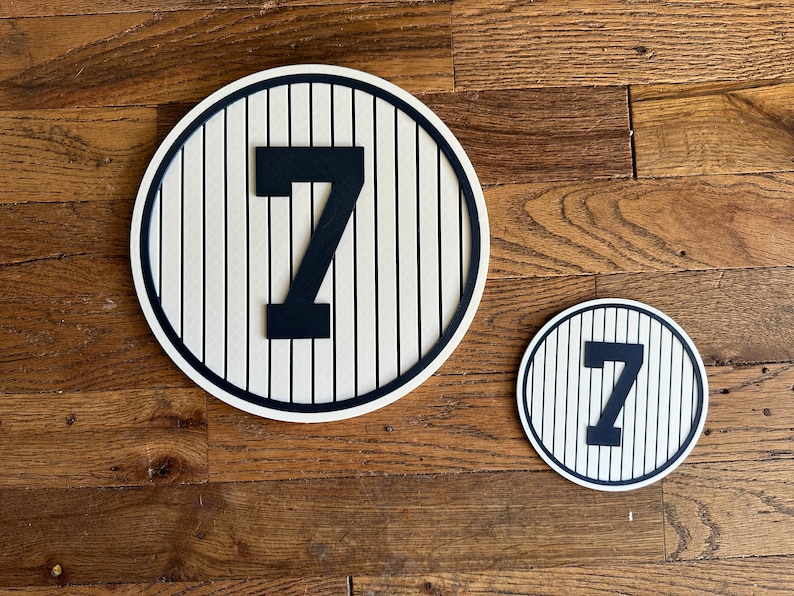 May include: Two round wooden signs with a baseball field design and the number "7" in black. The larger sign is approximately 12 inches in diameter and the smaller sign is approximately 6 inches in diameter.
