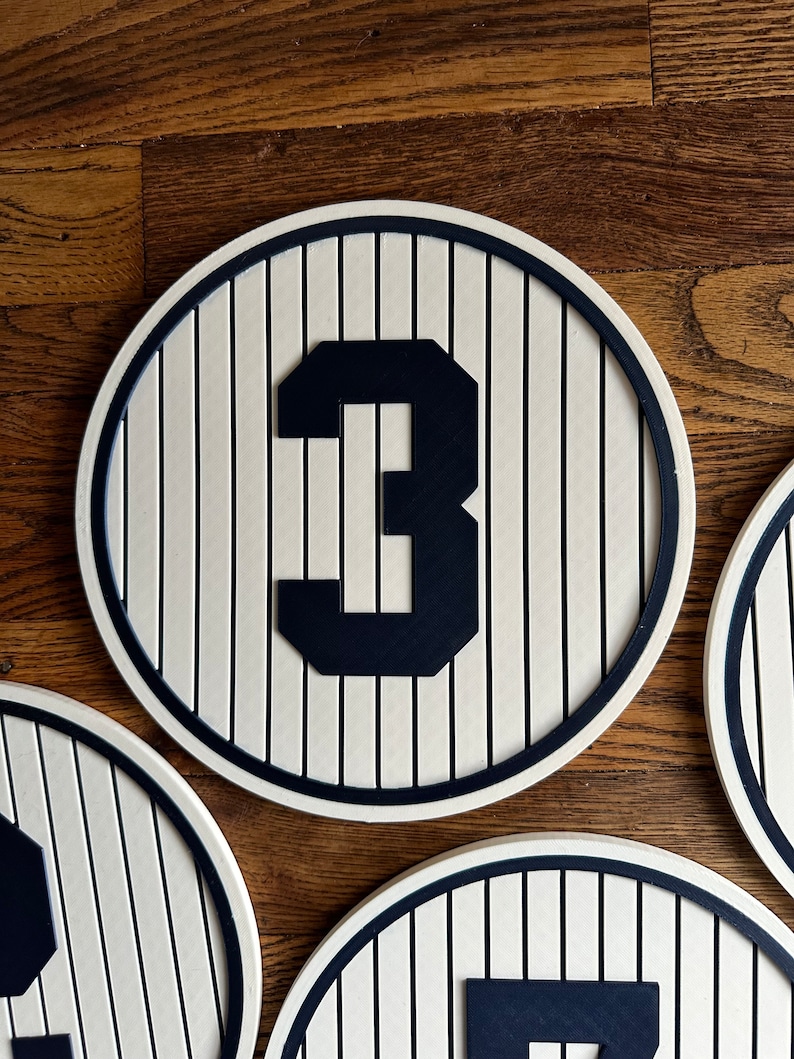 May include: A white and black circular sign with a black number "3" in the center. The sign has a striped pattern resembling a baseball field.