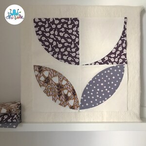 May include: A quilt block with four curved shapes, each with a different floral pattern. The shapes are arranged in a square pattern, with the top and bottom shapes being purple with white flowers, the left shape being brown with white flowers, and the right shape being gray with white dots.