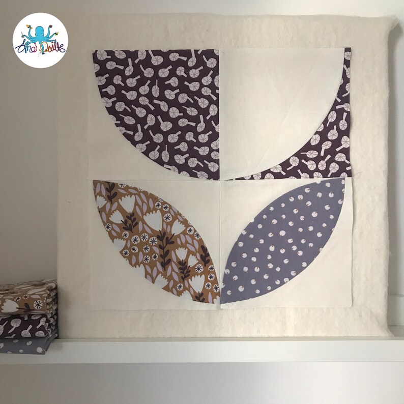 May include: A quilt block with four curved shapes, each with a different floral pattern. The shapes are arranged in a square pattern, with the top and bottom shapes being purple with white flowers, the left shape being brown with white flowers, and the right shape being gray with white dots.
