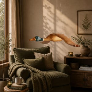 Puede incluir: Una escultura de madera de un pato en vuelo, suspendida del techo. El pato presenta tonos marrones, beige y azules, con las alas extendidas. La escultura cuelga sobre un sill&oacute;n verde, creando un dise&ntilde;o interior r&uacute;stico y acogedor.