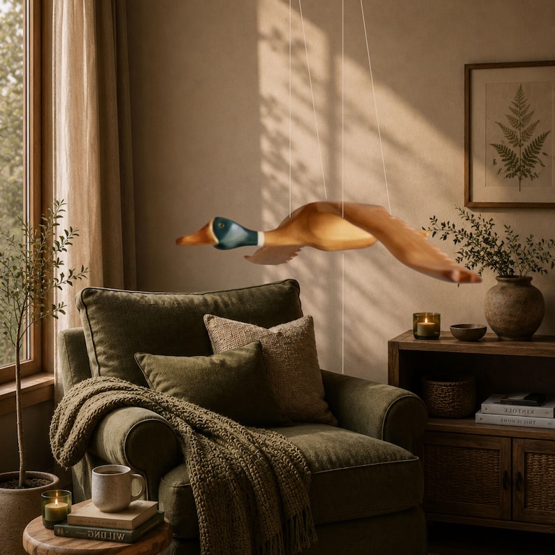 Puede incluir: Una escultura de madera de un pato en vuelo, suspendida del techo. El pato presenta tonos marrones, beige y azules, con las alas extendidas. La escultura cuelga sobre un sill&oacute;n verde, creando un dise&ntilde;o interior r&uacute;stico y acogedor.