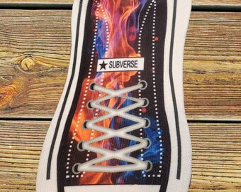 May include: A white sock with a black and white design of a sneaker with red and blue flames. The sock has the word "SUBVERSE" printed on it.