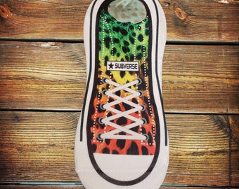 May include: A white sock with a colorful design of a leopard print with green, yellow, orange, and black colors. The sock has a white shoelace and the text "SUBVERSE" with a star on a white background.