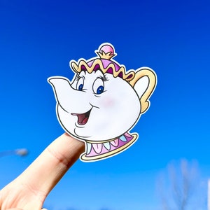 May include: A sticker of Mrs. Potts, the teapot character from Disney's Beauty and the Beast, with a pink and yellow dress and a white teapot body. The sticker is on a finger against a blue sky background.