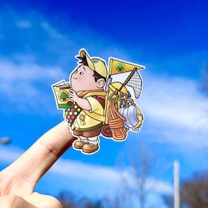 May include: A cartoon illustration of a young boy scout wearing a yellow uniform and a hat with a green tree logo. He is holding a book and has a backpack full of camping gear, including a rope, a net, and a canteen.