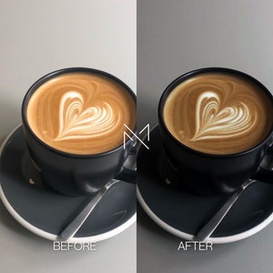 May include: A close-up of a black coffee cup with a heart-shaped design in the foam on top. The cup is on a gray saucer with a silver spoon.