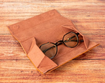 May include: A brown leather glasses case with a pair of tortoiseshell glasses inside. The case is open and the glasses are lying on the brown suede lining.