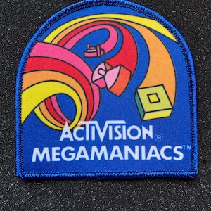 May include: A blue and yellow embroidered patch with a rainbow design and the text "Activision Megamanics".