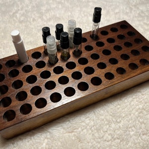 May include: A wooden organizer with 49 round holes for storing small bottles. The organizer is made of dark brown wood and has a smooth finish. There are 8 small bottles in the organizer, 7 with black caps and 1 with a white cap.