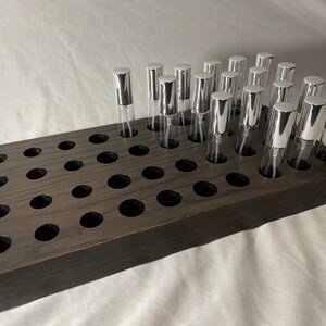 May include: A dark brown wooden tray with 42 holes for holding small bottles. The tray is filled with 20 silver spray bottles.