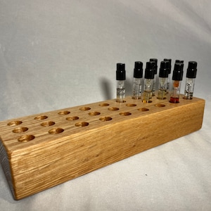 May include: A wooden stand with 36 holes for storing small perfume bottles. The stand is made of light brown wood and has a natural finish. There are 12 perfume bottles in the stand, all with black caps.