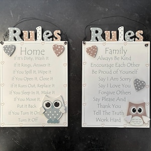Puede incluir: Dos letreros rectangulares de madera con la palabra "Reglas" en la parte superior. Un letrero dice "Hogar" y el otro "Familia", cada uno con una lista de reglas y un gráfico de búho. Los letreros son blancos con texto negro y corazones decorativos.